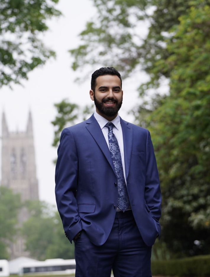Dmitri Morales outdoors in a navy suit, Duke Chapel behind him